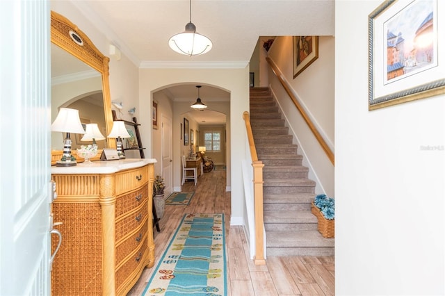 foyer entrance with baseboards, stairway, light wood-type flooring, ornamental molding, and arched walkways