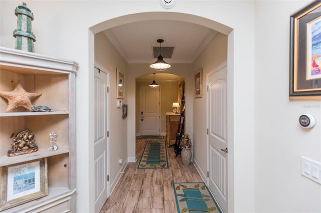 hall featuring light wood-type flooring, visible vents, arched walkways, crown molding, and baseboards