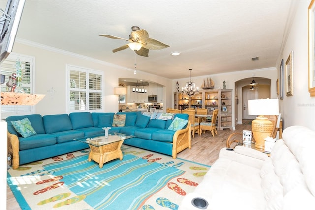 living area featuring light wood-style floors, crown molding, ceiling fan with notable chandelier, and arched walkways