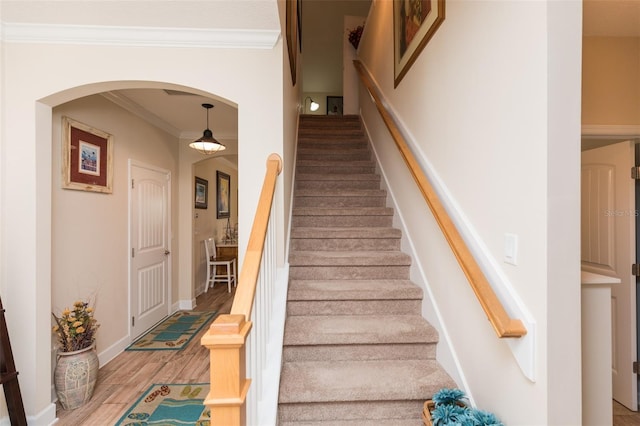 stairway with crown molding, wood finished floors, arched walkways, and baseboards