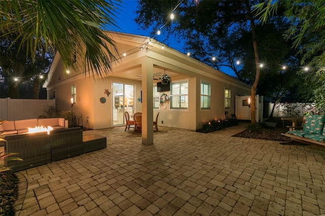 back of house at night with stucco siding, a patio, fence, an outdoor living space with a fire pit, and ceiling fan