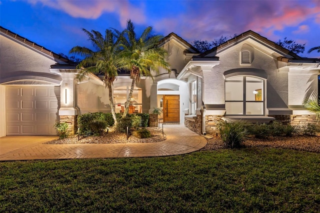 view of front of home with an attached garage, stone siding, a lawn, and stucco siding