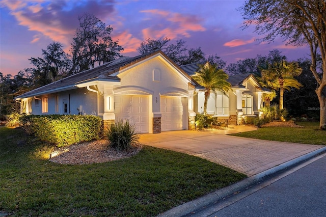 view of front of home with a lawn, stone siding, an attached garage, decorative driveway, and stucco siding