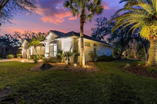 property exterior at dusk featuring driveway, a lawn, an attached garage, and stucco siding