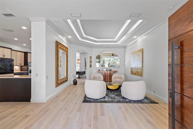 sitting room featuring light wood finished floors, visible vents, arched walkways, and a tray ceiling