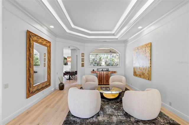 living area with light wood finished floors, baseboards, arched walkways, a raised ceiling, and crown molding