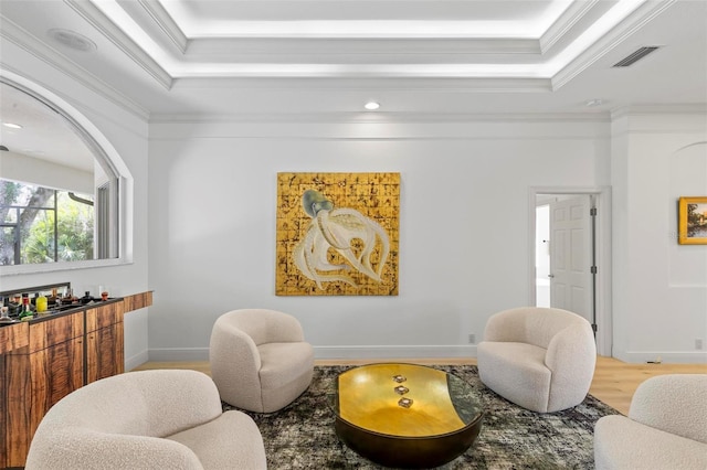 sitting room featuring wood finished floors, visible vents, baseboards, a raised ceiling, and crown molding