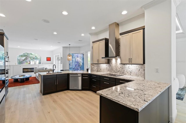 kitchen featuring a peninsula, a sink, open floor plan, wall chimney range hood, and light wood finished floors