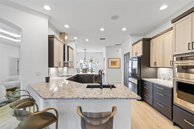 kitchen with ornamental molding, light stone counters, a peninsula, double oven, and a sink