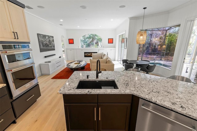 kitchen featuring light stone counters, stainless steel appliances, crown molding, light wood-style floors, and a sink