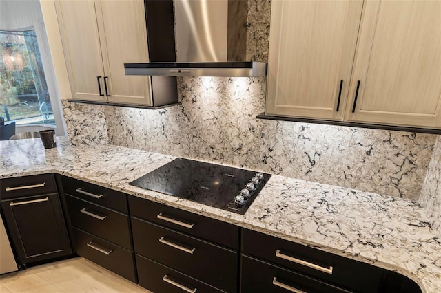 kitchen with wall chimney exhaust hood, black electric stovetop, backsplash, and light stone counters