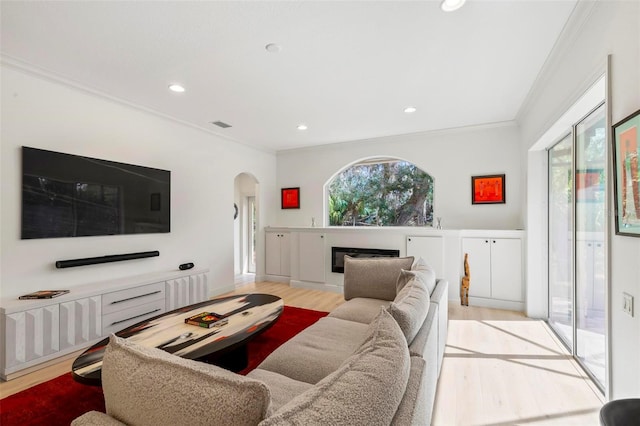 living area featuring arched walkways, a healthy amount of sunlight, wood finished floors, and crown molding