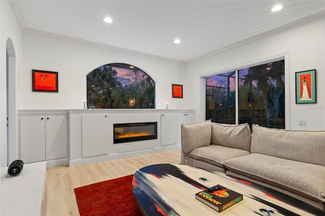 living room with ornamental molding, wood finished floors, a glass covered fireplace, and recessed lighting