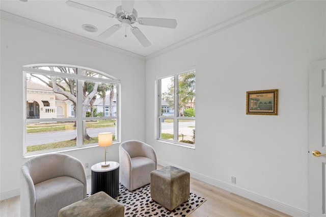 living area with ornamental molding, baseboards, ceiling fan, and light wood finished floors