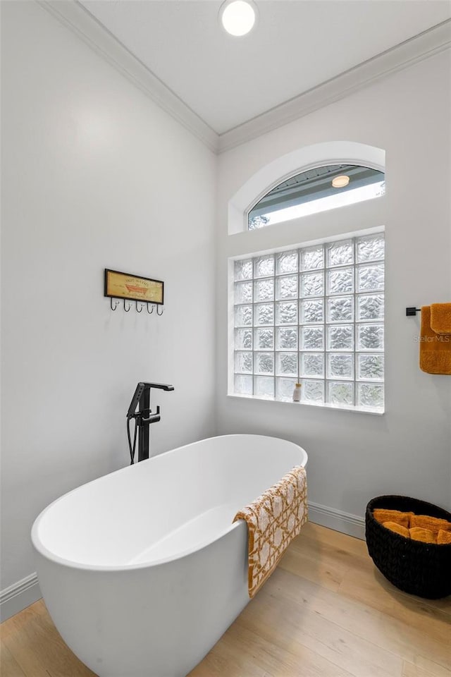 full bath with a freestanding tub, baseboards, ornamental molding, and wood finished floors