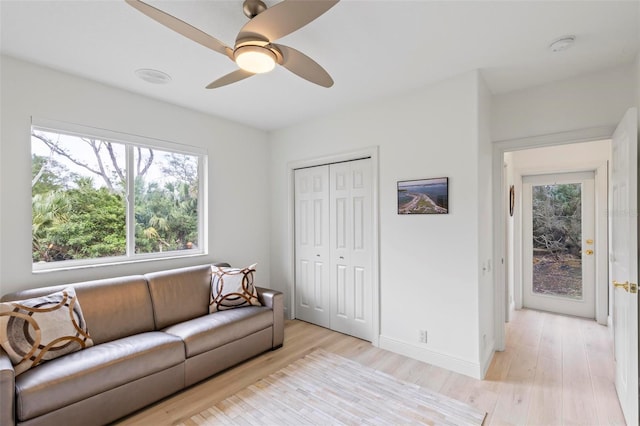 living area featuring ceiling fan, light wood-style flooring, and baseboards