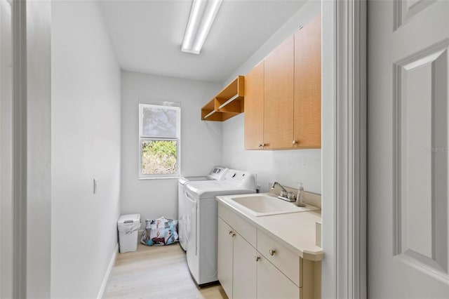 clothes washing area featuring light wood-style flooring, independent washer and dryer, a sink, and cabinet space