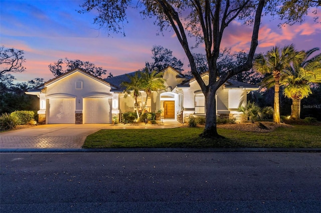 view of front of home with stucco siding, a front yard, decorative driveway, and a garage