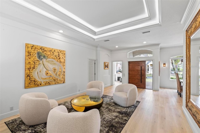 living area featuring light wood finished floors, crown molding, and a raised ceiling