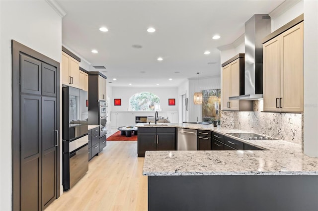 kitchen with wall chimney range hood, light stone counters, a peninsula, black appliances, and a sink