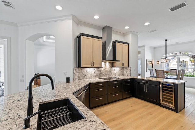 kitchen featuring wine cooler, visible vents, wall chimney range hood, and a sink