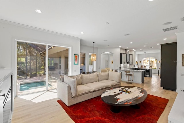 living area featuring visible vents, crown molding, recessed lighting, light wood-style floors, and arched walkways