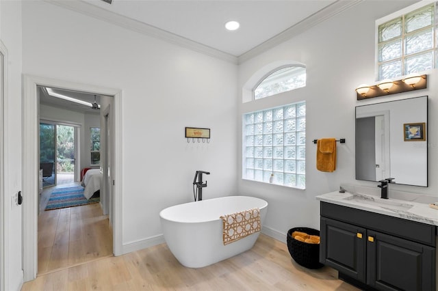 ensuite bathroom with a soaking tub, a healthy amount of sunlight, wood finished floors, and ornamental molding