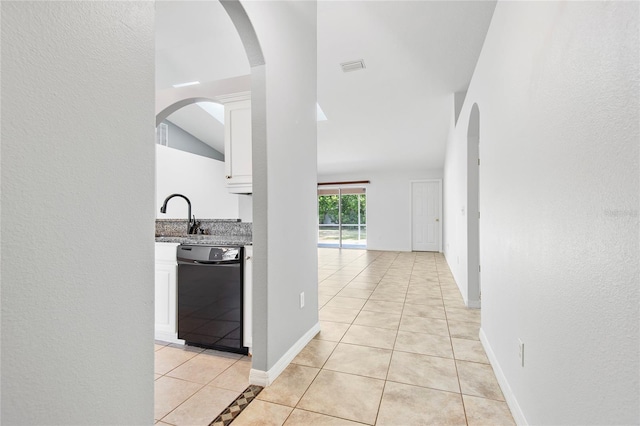 hallway featuring light tile patterned floors, arched walkways, a sink, and baseboards