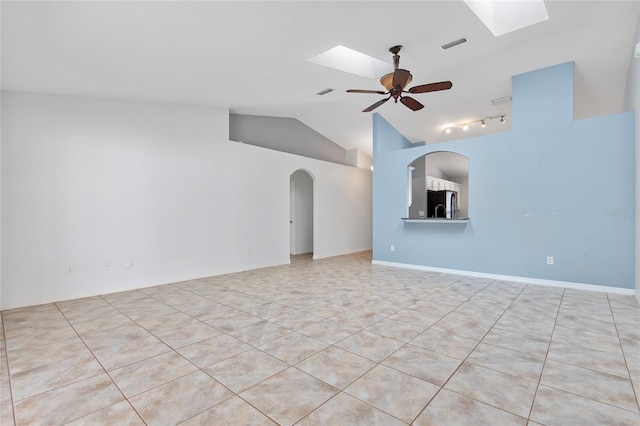 spare room with baseboards, vaulted ceiling with skylight, arched walkways, and a ceiling fan