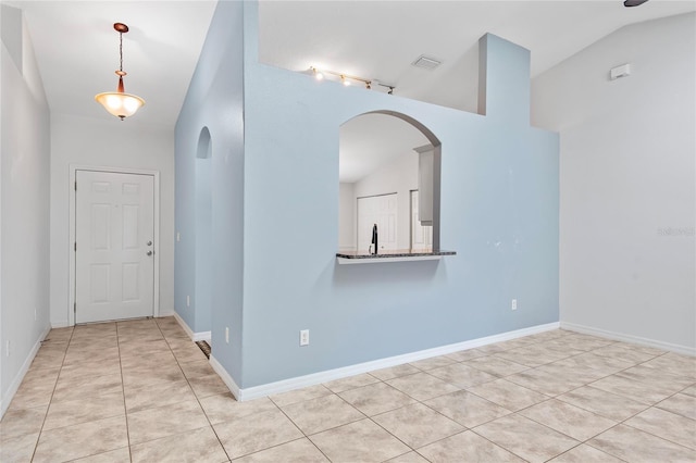 tiled spare room with lofted ceiling, visible vents, arched walkways, and baseboards