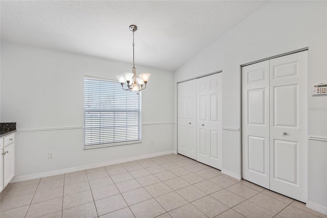 unfurnished dining area with a notable chandelier, vaulted ceiling, a textured ceiling, and light tile patterned floors