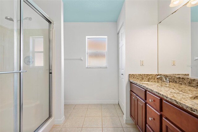 bathroom featuring double vanity, a stall shower, a sink, tile patterned flooring, and baseboards