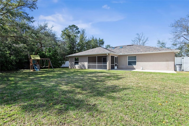 rear view of house featuring a yard, a playground, and stucco siding