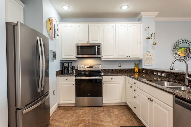 kitchen featuring appliances with stainless steel finishes, ornamental molding, a sink, a textured ceiling, and dark stone countertops