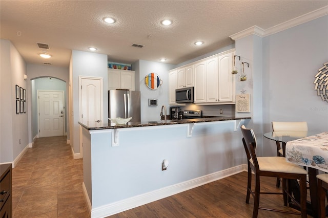 kitchen with arched walkways, a breakfast bar area, appliances with stainless steel finishes, dark stone countertops, and a peninsula