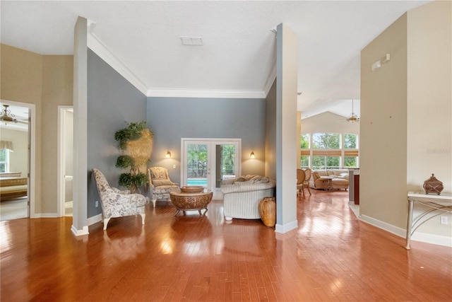 living area with ornamental molding, a ceiling fan, wood finished floors, baseboards, and vaulted ceiling