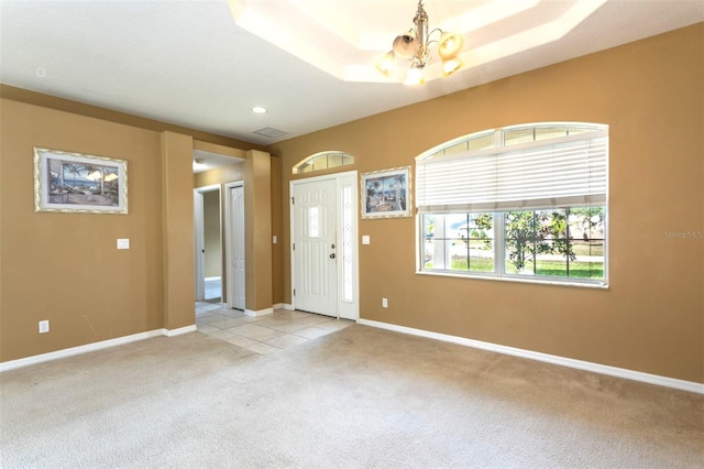 foyer with visible vents, baseboards, light colored carpet, a tray ceiling, and a notable chandelier