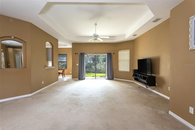 unfurnished living room with a tray ceiling, carpet flooring, visible vents, and baseboards