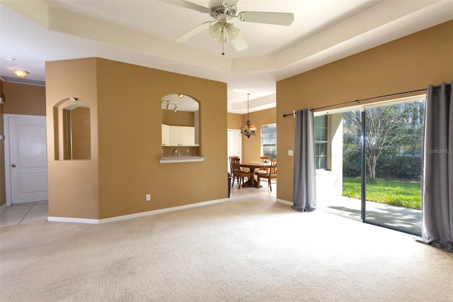 spare room with light carpet, ceiling fan with notable chandelier, and baseboards