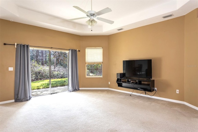 unfurnished living room with carpet floors, a raised ceiling, visible vents, and baseboards