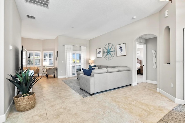 tiled living area with arched walkways, visible vents, a textured ceiling, and baseboards