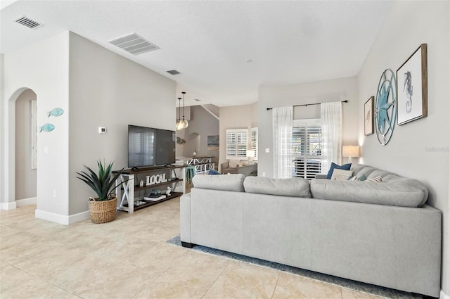 living area with light tile patterned floors, visible vents, arched walkways, and baseboards