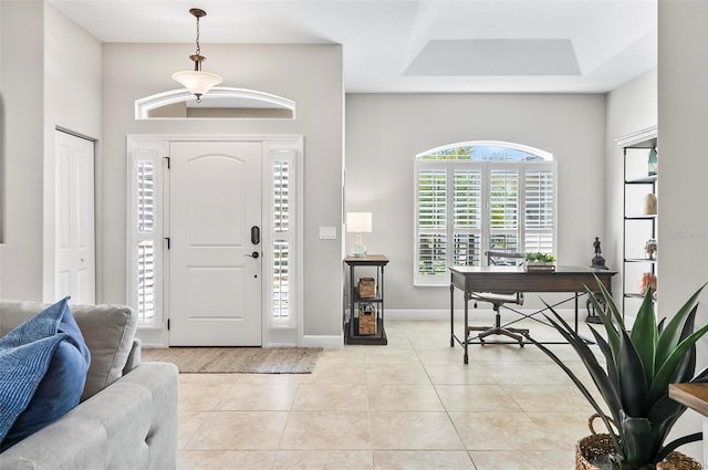 foyer entrance with a raised ceiling, light tile patterned floors, and baseboards