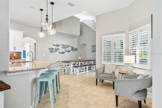 kitchen with light stone counters, visible vents, arched walkways, white cabinets, and a kitchen bar