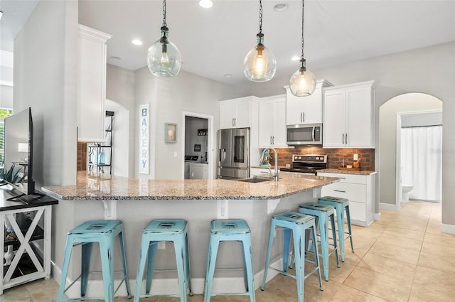 kitchen with light stone countertops, arched walkways, a sink, appliances with stainless steel finishes, and backsplash