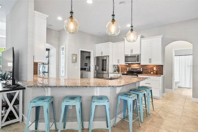 kitchen featuring a sink, light stone counters, stainless steel appliances, arched walkways, and decorative backsplash