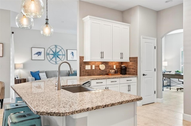 kitchen featuring light stone countertops, a breakfast bar, arched walkways, a sink, and decorative backsplash