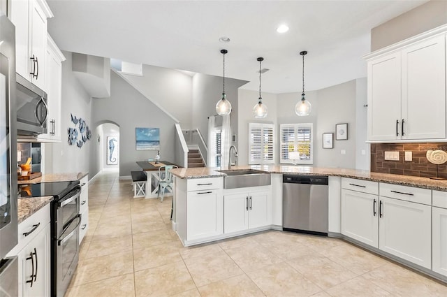 kitchen with a sink, light stone counters, backsplash, arched walkways, and appliances with stainless steel finishes