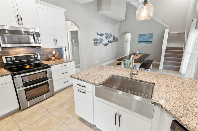 kitchen with a sink, tasteful backsplash, stainless steel appliances, arched walkways, and white cabinets