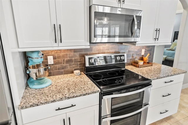 kitchen with stainless steel appliances, light stone countertops, and white cabinets